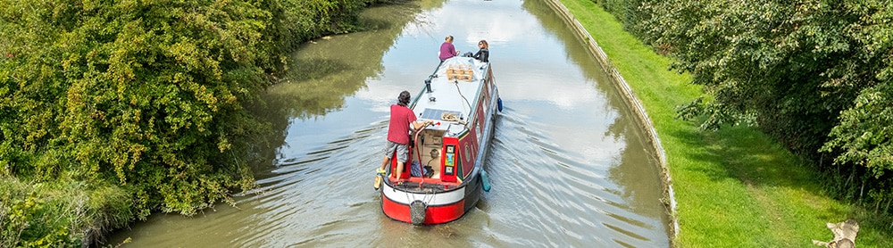 Canal boat sailing on a canal surrounded by trees