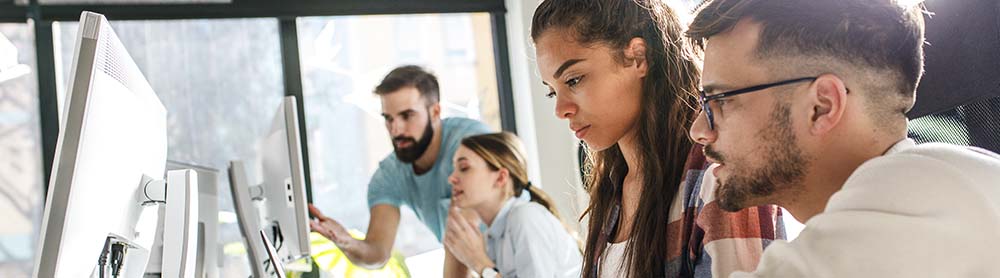 Co-workers working and talking in front of computer screens 