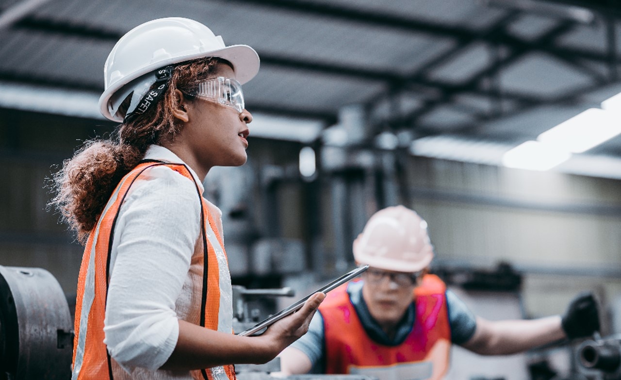 Two individuals wearing safety vests and hard hats in an industrial setting