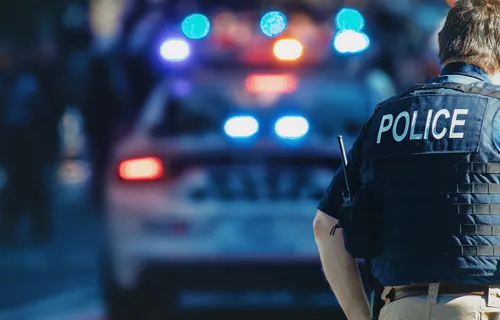 Polizist in Schutzweste vor Einsatzfahrzeug mit Blaulicht