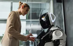 Woman in blazer interacts with humanoid robot in an office setting.