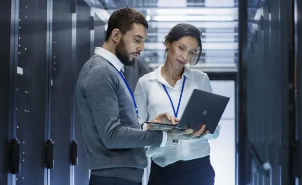 Consultants working in on a laptop in a server room discussing CGI SiteReliability360