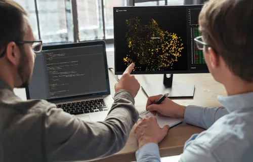 two AI experts looking at models on computer monitor
