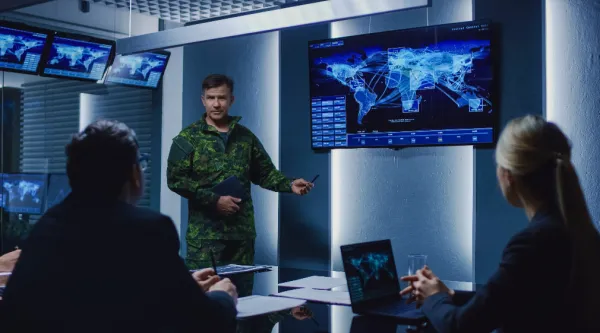Military personnel meeting in front of monitors and a laptop