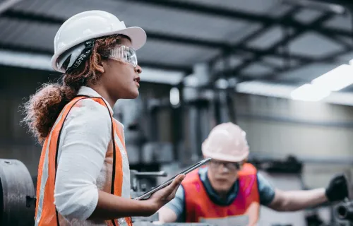 Two individuals wearing safety vests and hard hats in an industrial setting