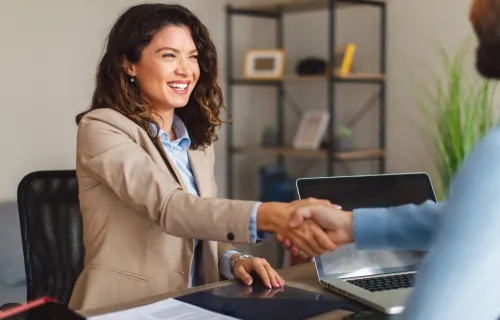 Two professionals smiling and shaking hands across a desk