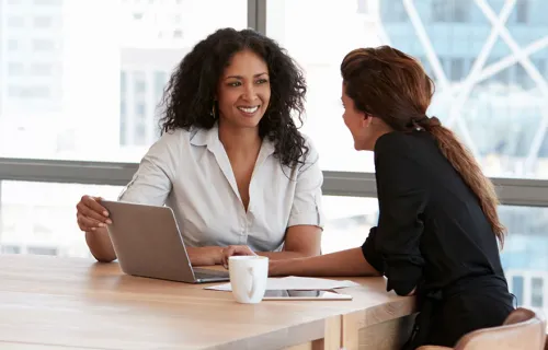 Two women sit in an office using a laptop